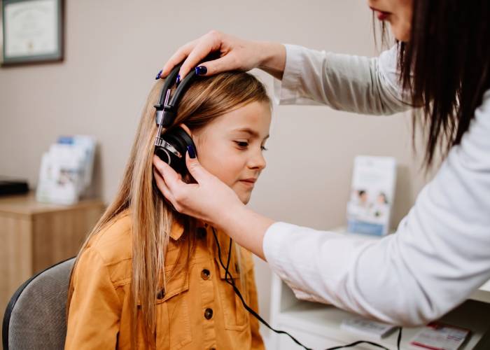 A woman gently listens to a child's ear, showing concern and care in a nurturing environment.