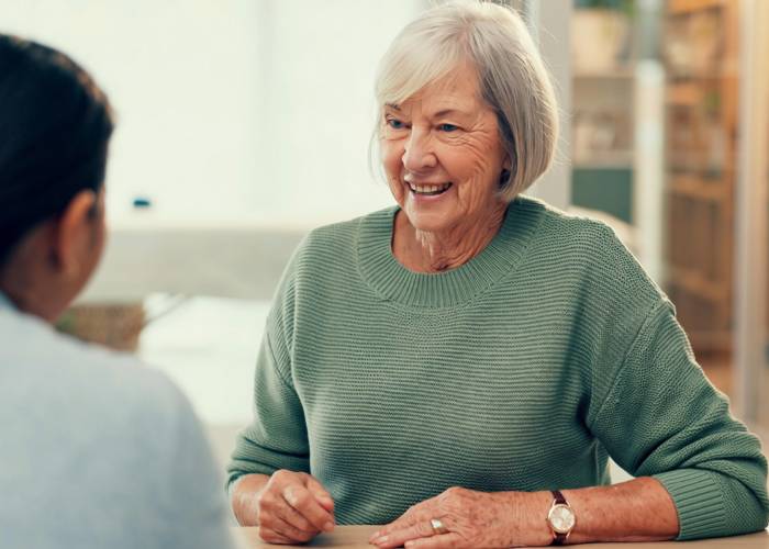 A woman converses with an older woman at a table, both engaged in a thoughtful discussion.