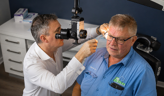 Eye care professional examines an older man's eye with a slit-lamp microscope in a clinic, conveying careful, compassionate medical attention.