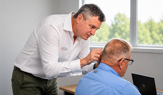 Healthcare professional examines an older man's scalp during a consultation in a bright office, with a laptop nearby, conveying attentive medical care.