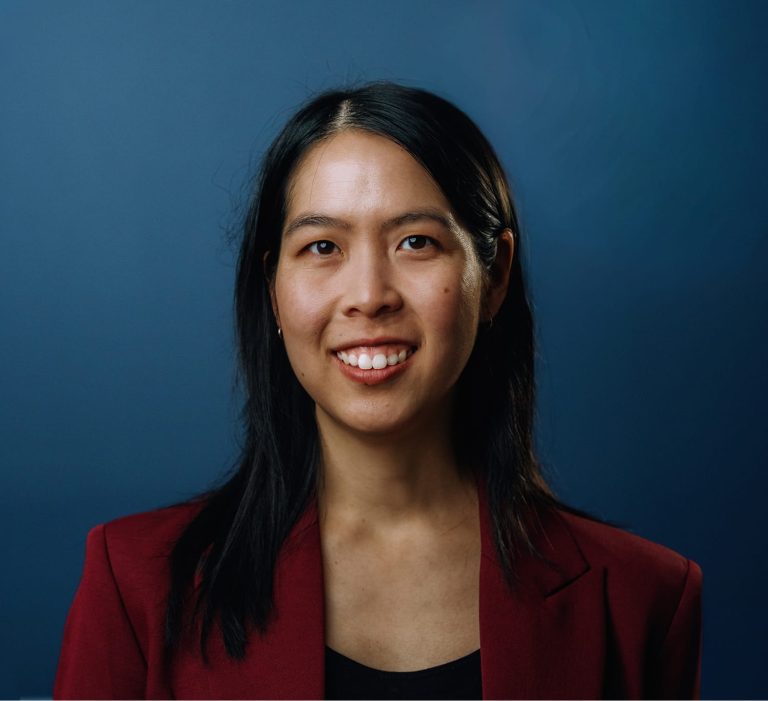 A woman wearing a red blazer over a black shirt smiles warmly at the camera.