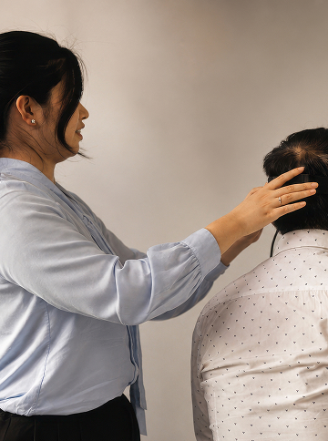 Man wearing a VR headset looks at a large screen displaying a close-up of an eye while a person adjusts the headset.