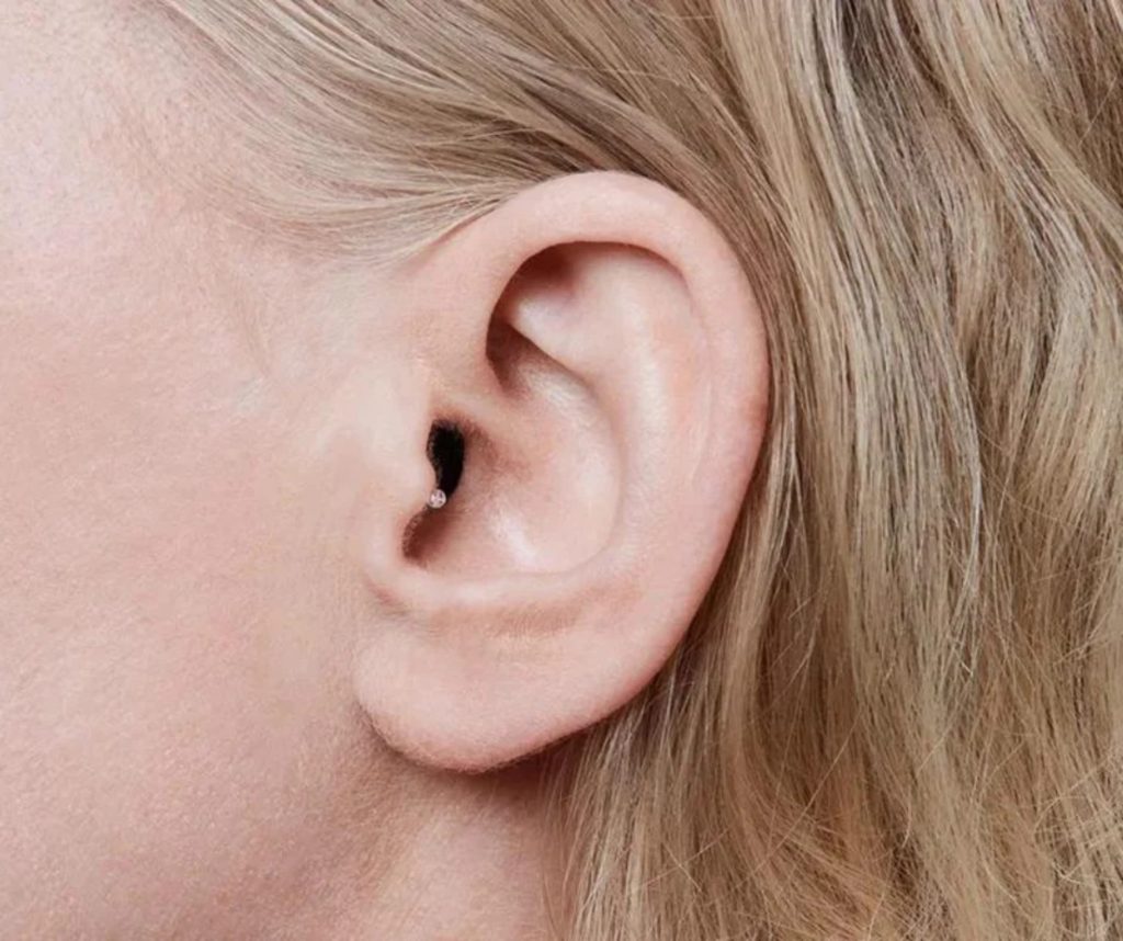 Close-up of a person's ear with blonde hair, showing a small diamond stud piercing in the tragus.